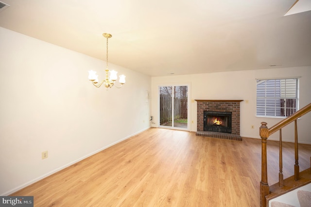 unfurnished living room featuring baseboards, wood finished floors, stairs, a brick fireplace, and a chandelier