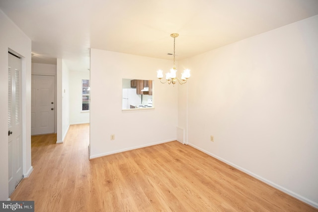 empty room featuring light wood-style flooring, a chandelier, and baseboards