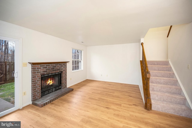 unfurnished living room featuring a brick fireplace, stairs, baseboards, and wood finished floors