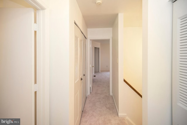 hallway featuring baseboards, an upstairs landing, and light colored carpet