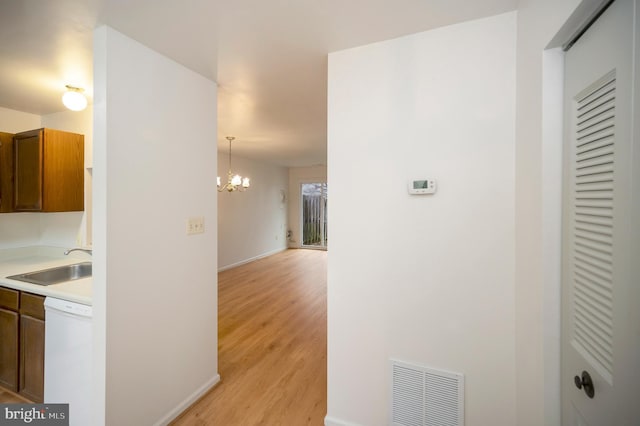 hallway featuring a chandelier, a sink, visible vents, baseboards, and light wood-type flooring