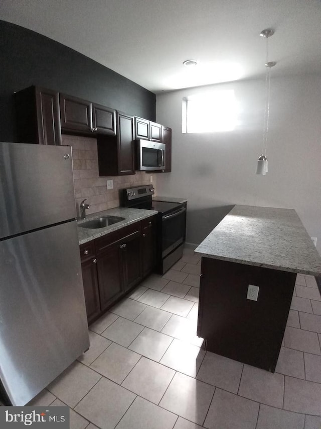 kitchen featuring light tile patterned flooring, dark brown cabinetry, a sink, appliances with stainless steel finishes, and tasteful backsplash