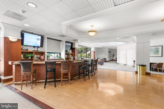 bar featuring a bar, decorative columns, a tray ceiling, and wood finished floors