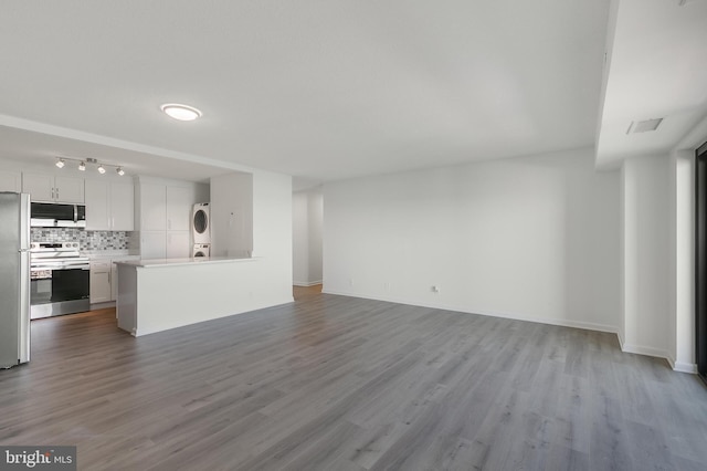 unfurnished living room featuring stacked washing maching and dryer, wood finished floors, and visible vents