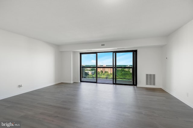 empty room featuring dark wood-style floors, visible vents, and baseboards