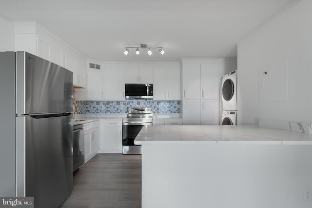 kitchen featuring stacked washer and dryer, appliances with stainless steel finishes, a peninsula, and white cabinets