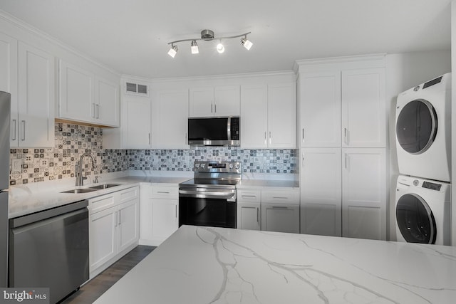 kitchen with stainless steel appliances, stacked washer / dryer, a sink, white cabinets, and decorative backsplash