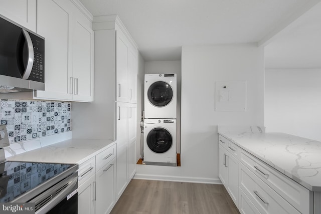 laundry room with light wood-type flooring, stacked washer / drying machine, and baseboards