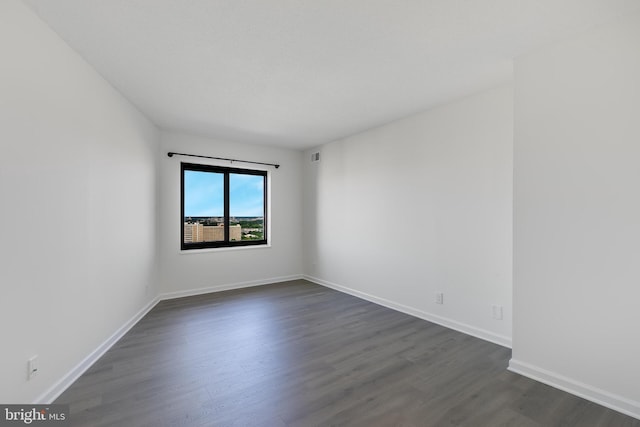 empty room featuring dark wood-type flooring, visible vents, and baseboards