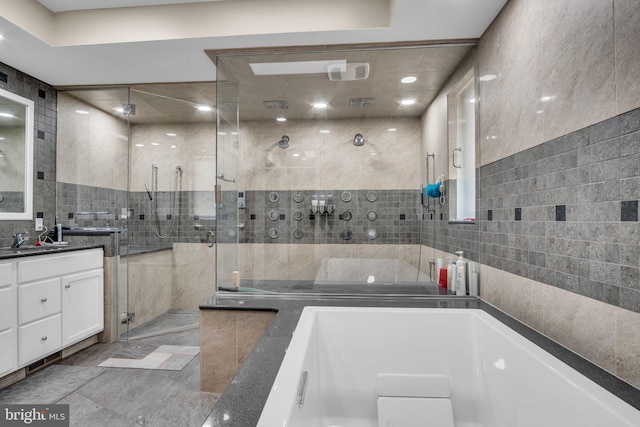 full bathroom with a tub to relax in, a stall shower, vanity, and tile walls