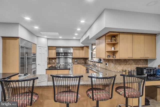 kitchen featuring stainless steel appliances, decorative backsplash, a sink, wall chimney range hood, and a peninsula