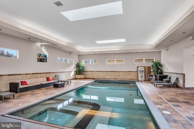 view of swimming pool featuring a skylight and a pool with connected hot tub