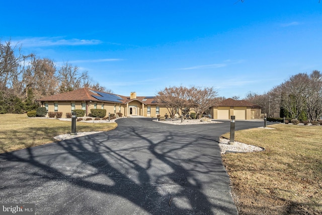 ranch-style house with a garage, stucco siding, solar panels, and a front yard