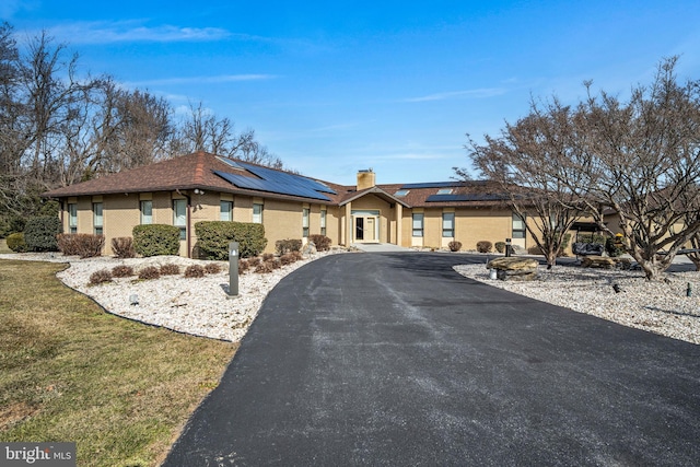 ranch-style home featuring brick siding, driveway, roof mounted solar panels, a chimney, and a front yard