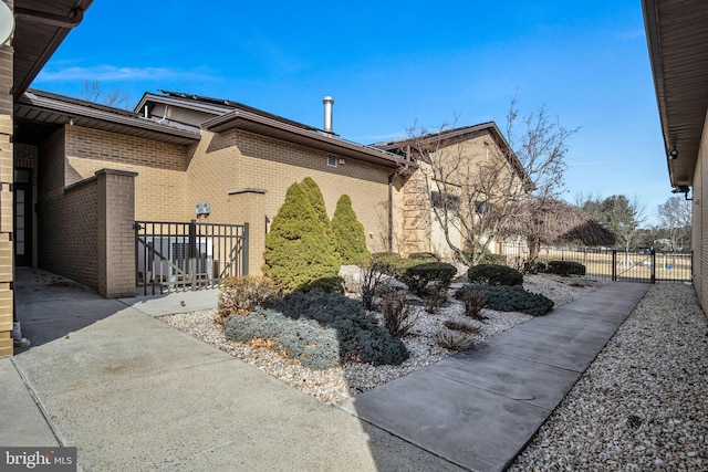 view of home's exterior with a gate, brick siding, and fence