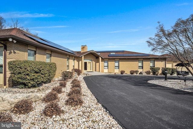 ranch-style house with solar panels, brick siding, and a chimney