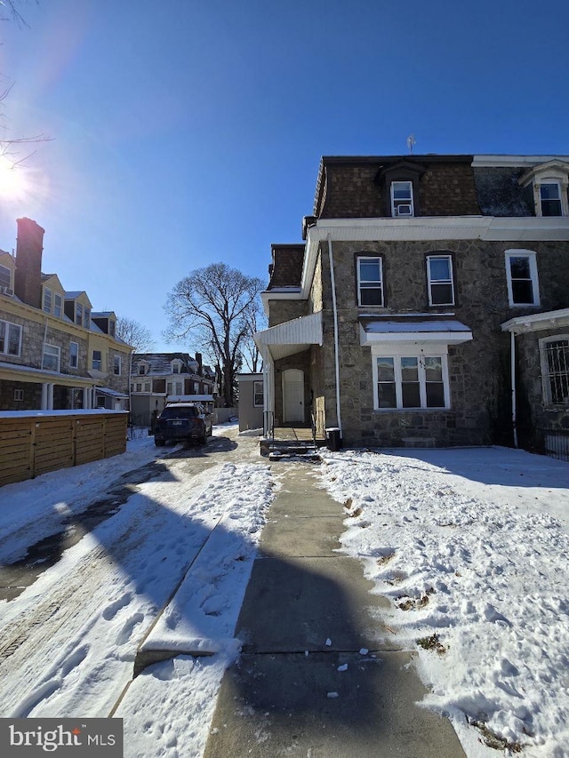 snow covered property with fence and mansard roof