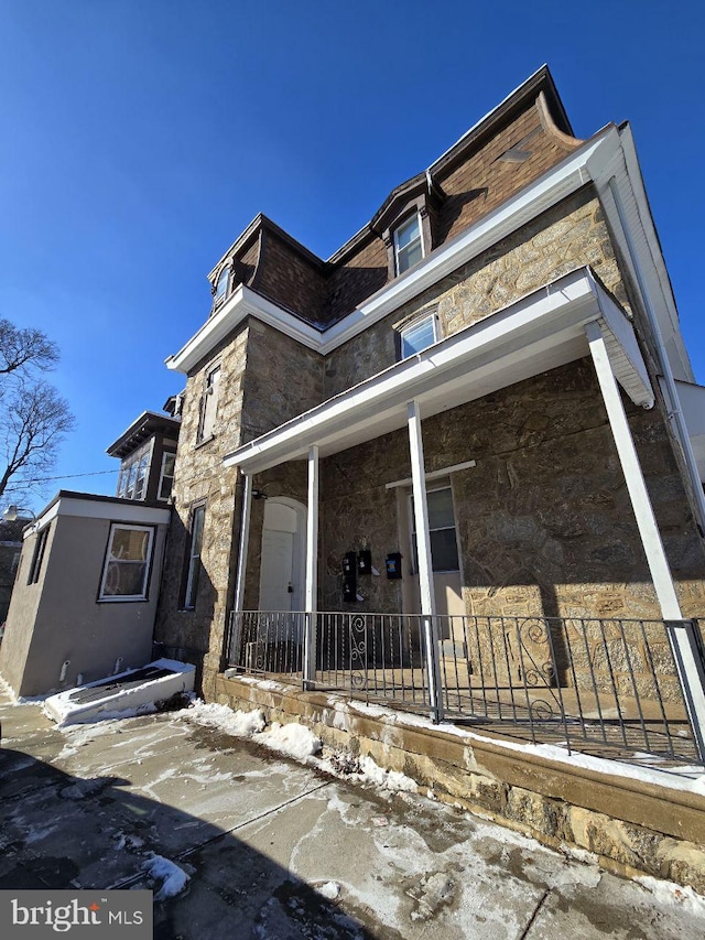 view of side of home with covered porch and stone siding