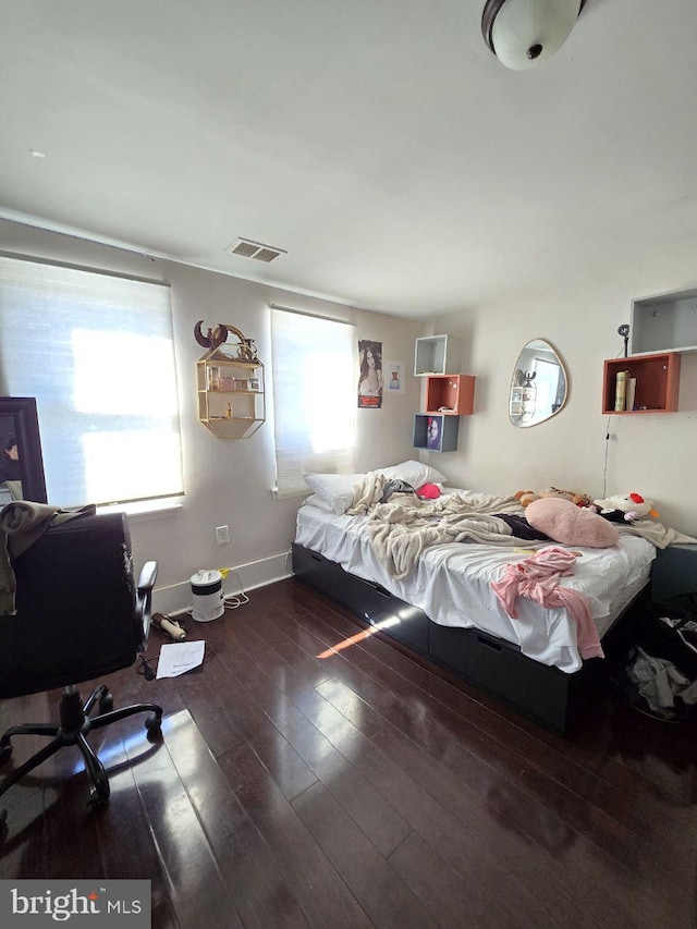 bedroom featuring hardwood / wood-style floors, multiple windows, visible vents, and baseboards