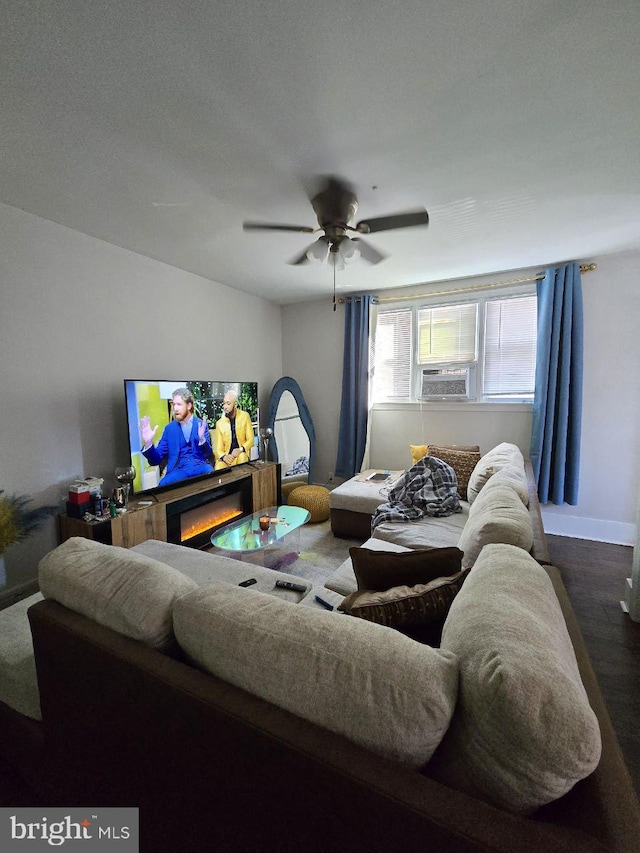 living area featuring a warm lit fireplace, ceiling fan, cooling unit, wood finished floors, and baseboards