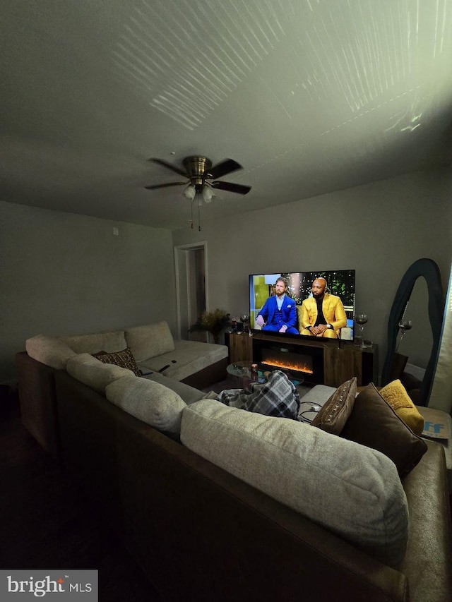 living room featuring a ceiling fan and a warm lit fireplace