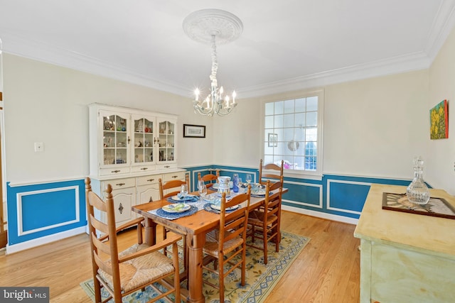 dining space featuring light wood-style flooring, a wainscoted wall, ornamental molding, and a chandelier