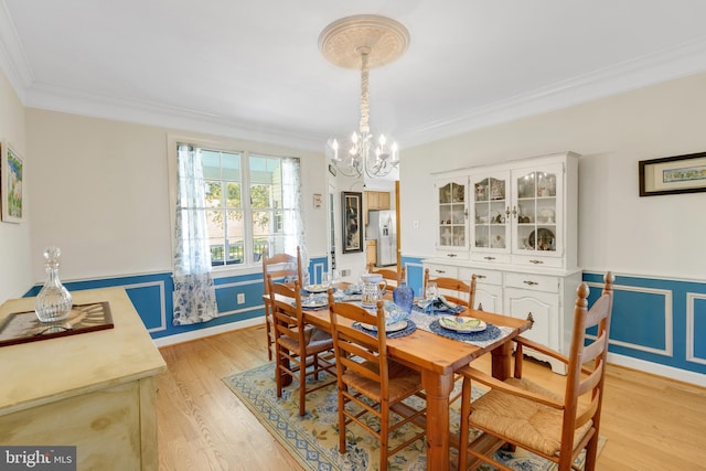 dining space featuring an inviting chandelier, crown molding, light wood-style flooring, and wainscoting