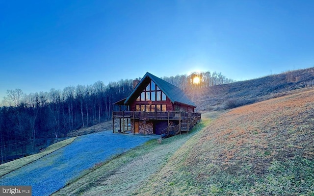 back of property featuring a chimney, a lawn, stone siding, driveway, and a wooden deck