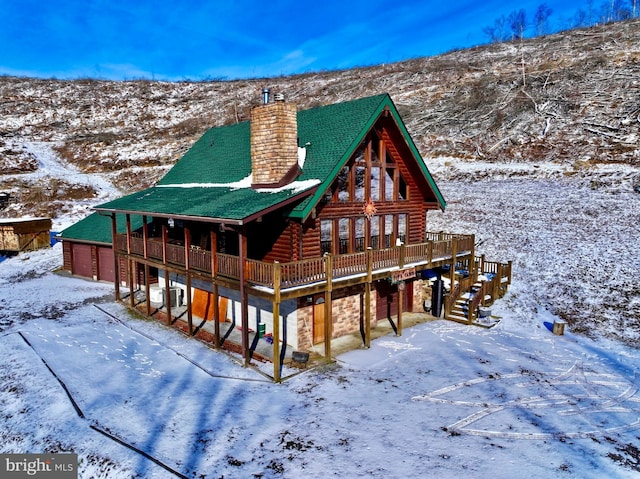 snow covered property featuring a chimney, log exterior, a deck, a garage, and stone siding