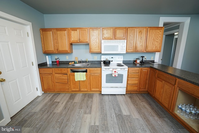 kitchen featuring white appliances, dark countertops, light wood-style flooring, brown cabinets, and a sink