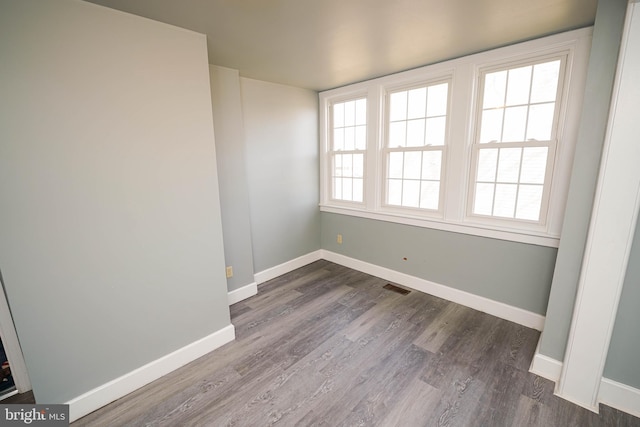 empty room with wood finished floors, visible vents, and baseboards