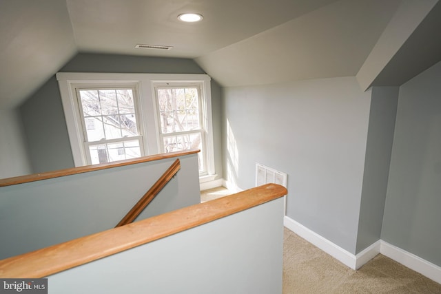 hall featuring lofted ceiling, light colored carpet, visible vents, an upstairs landing, and baseboards