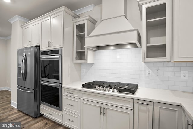 kitchen featuring dark wood-style floors, decorative backsplash, appliances with stainless steel finishes, ornamental molding, and premium range hood