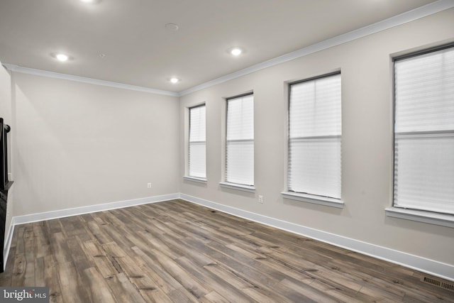 spare room with baseboards, visible vents, wood finished floors, and ornamental molding