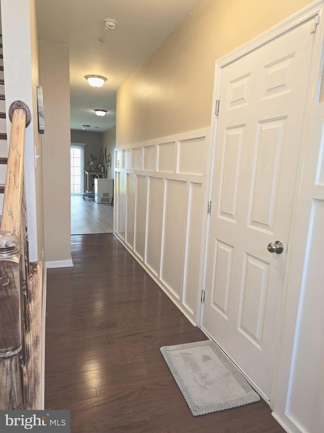 hall with dark wood-style floors, a wainscoted wall, and a decorative wall