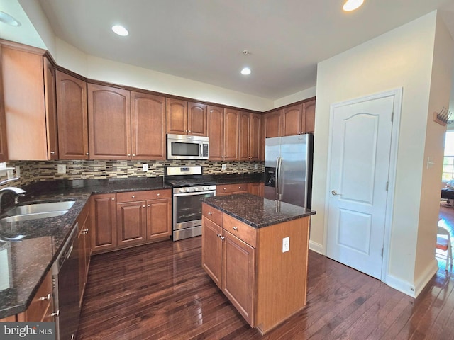 kitchen featuring dark wood-type flooring, a kitchen island, a sink, appliances with stainless steel finishes, and tasteful backsplash