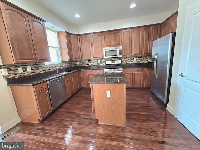 kitchen featuring dark wood-style flooring, a sink, appliances with stainless steel finishes, a center island, and dark stone countertops