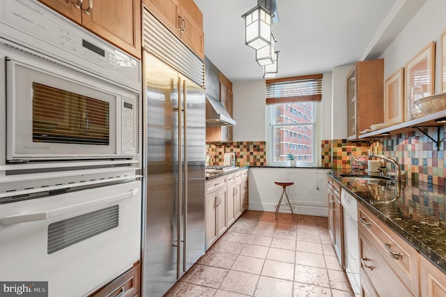 kitchen with stainless steel appliances, a sink, hanging light fixtures, decorative backsplash, and dark stone countertops