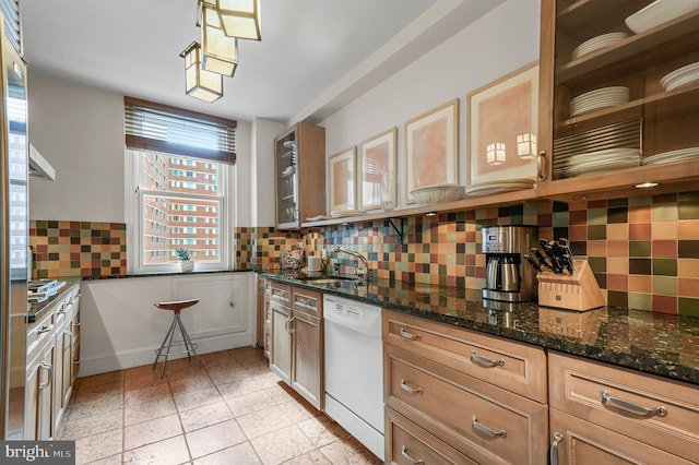 kitchen featuring white dishwasher, dark stone counters, decorative backsplash, and a sink