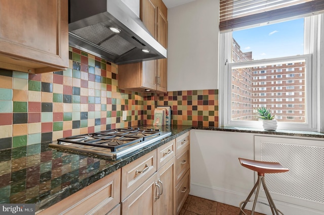 kitchen with stainless steel gas cooktop, decorative backsplash, tile patterned floors, wall chimney exhaust hood, and radiator