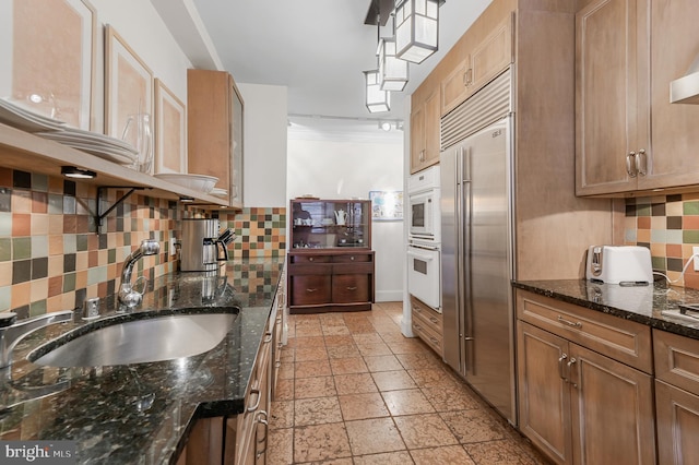 kitchen featuring built in fridge, a sink, white oven, backsplash, and stone tile flooring