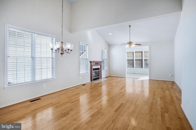 unfurnished living room with light wood finished floors, visible vents, a fireplace with flush hearth, high vaulted ceiling, and ceiling fan with notable chandelier