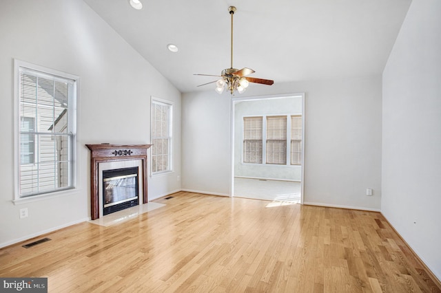 unfurnished living room with lofted ceiling, ceiling fan, wood finished floors, visible vents, and a tiled fireplace