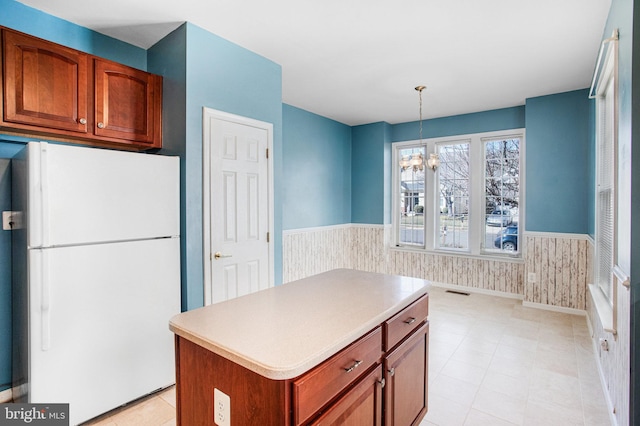 kitchen with a wainscoted wall, brown cabinets, freestanding refrigerator, and a center island