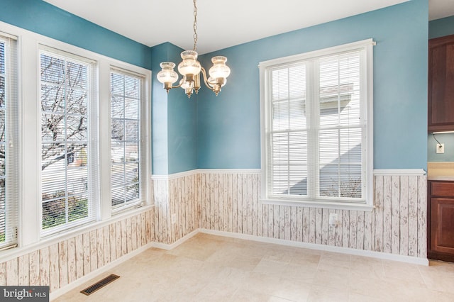 unfurnished dining area featuring a wainscoted wall, visible vents, and wallpapered walls