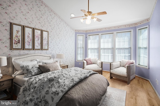 bedroom featuring vaulted ceiling, light wood finished floors, baseboards, and wallpapered walls