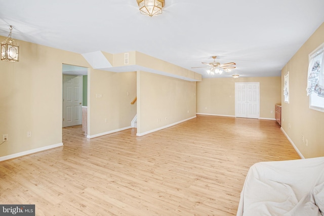 unfurnished living room with ceiling fan with notable chandelier, light wood-type flooring, baseboards, and stairs