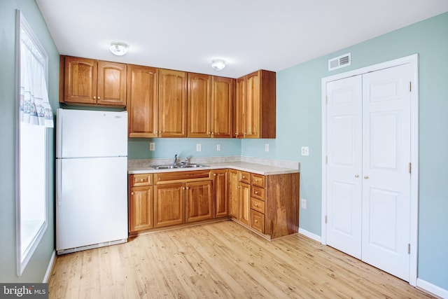 kitchen featuring light countertops, visible vents, brown cabinetry, freestanding refrigerator, and a sink