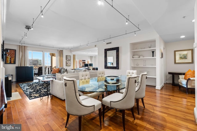 dining room featuring built in shelves, rail lighting, and light wood-style flooring