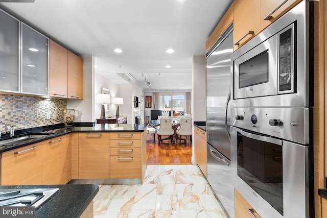 kitchen with built in appliances, a peninsula, a sink, marble finish floor, and decorative backsplash